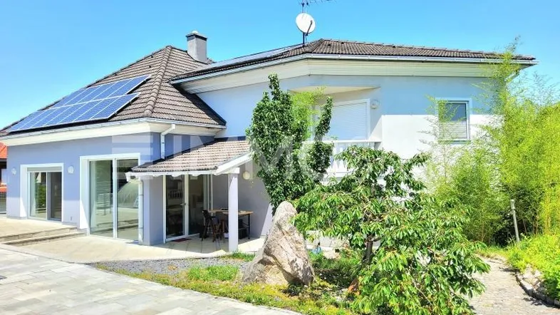 Modernes Haus mit Solaranlage, großen Glasfronten und überdachter Terrasse im Grünen.