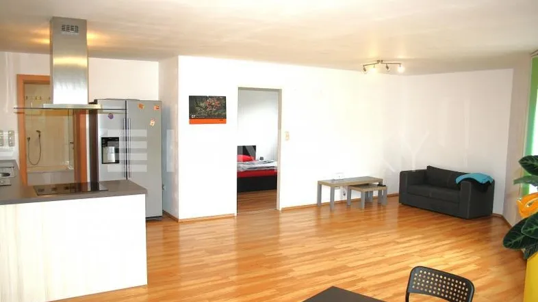Heller offener Wohnbereich mit integrierter Küche, Holzboden und Blick in ein Schlafzimmer.