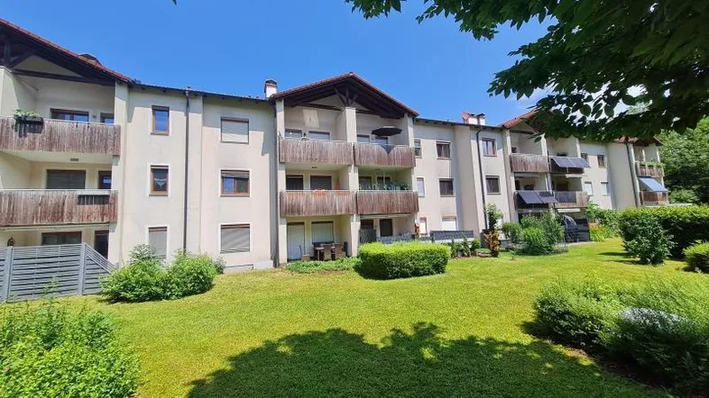 Mehrfamilienhaus mit mehreren Balkonen und gepflegter Grünfläche im Vordergrund.
