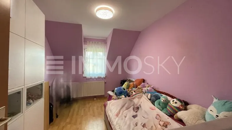 Gemütliches Kinderzimmer mit rosa Wänden, Holzboden und Dachschrägenfenster.