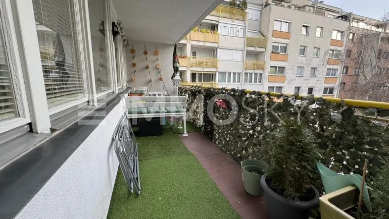 Balkon mit Kunstrasen, Pflanzen und Blick auf umliegende Wohngebäude in städtischer Umgebung.