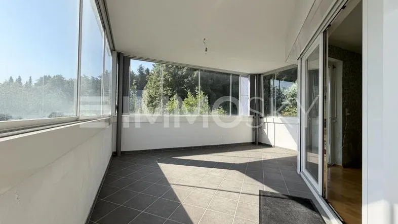 Helle, verglaste Loggia mit Fliesenboden und Blick ins Grüne, ideal zum Entspannen.