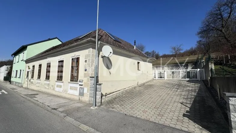 Altes Gebäude mit heller Fassade und gepflasterter Einfahrt unter blauem Himmel.