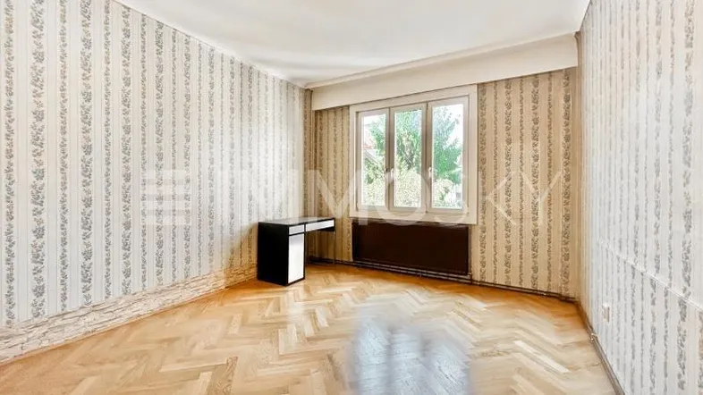 Helles Zimmer mit Fischgrätparkettboden, gemusterter Tapete und Blick ins Grüne.