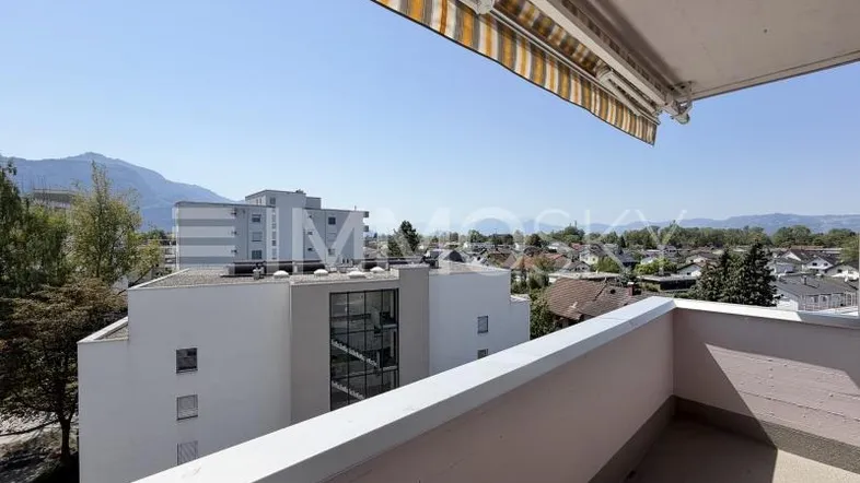Balkon mit Markise und weitem Blick über die Stadt auf Berge und See.