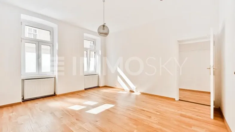 Helles Zimmer mit Parkettboden, weißen Wänden und viel Tageslicht durch große Fenster.