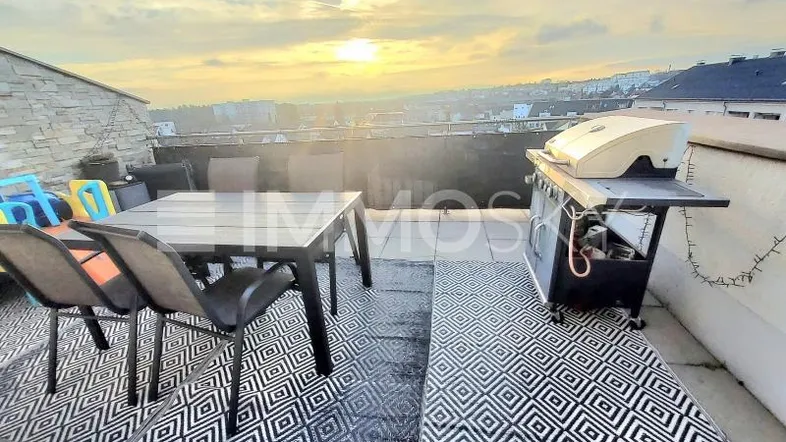 Große Dachterrasse mit Esstisch, Grill und Blick über die Stadt bei Sonnenuntergang.