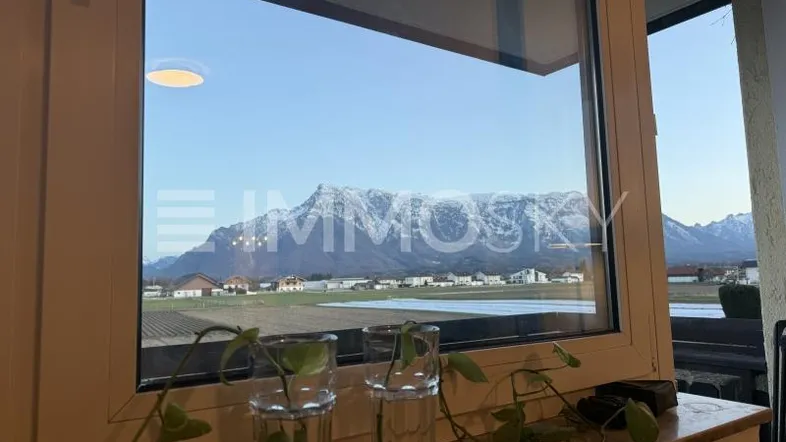 Panoramablick aus dem Fenster auf schneebedeckte Berge und weite Felder bei Sonnenuntergang.