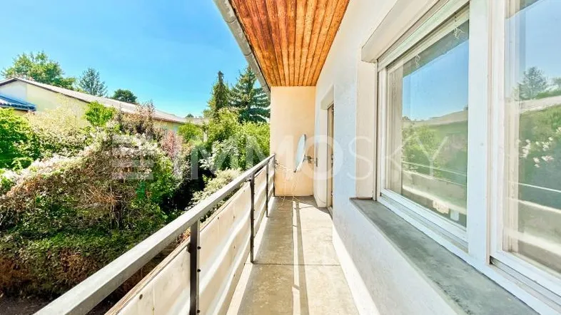Heller Balkon mit Holzdecke, Metallgeländer und Blick ins Grüne.