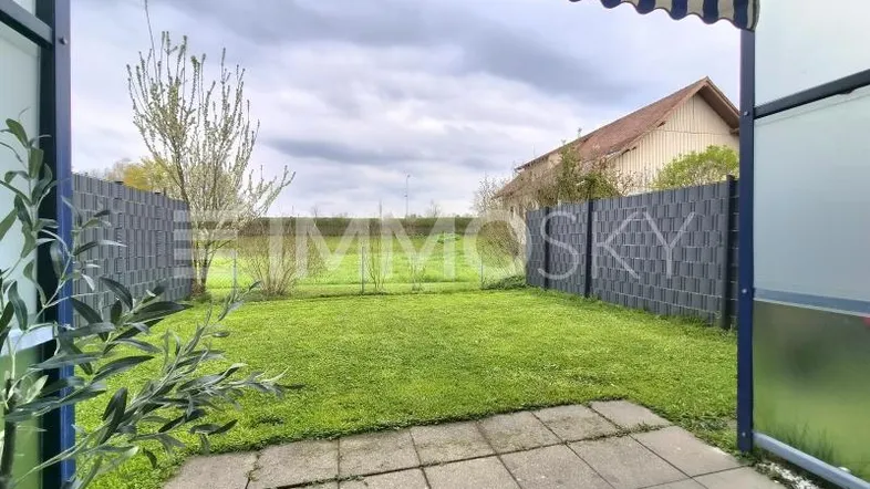 Gepflasterte Terrasse mit Markise und Blick auf den privaten Gartenbereich mit Rasenfläche.
