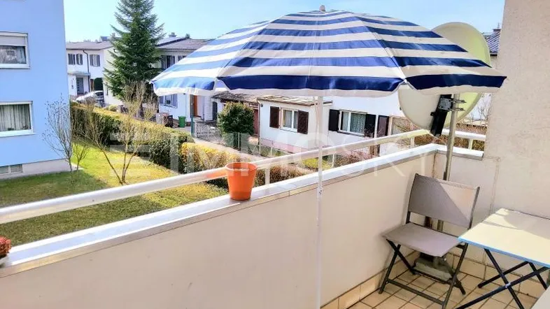Gemütlicher Balkon mit blau-weiß gestreiftem Sonnenschirm und Blick auf die Umgebung.