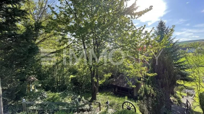 Üppiger grüner Garten mit altem Baumbestand, einer kleinen Hütte und weitem Blick in die Landschaft.