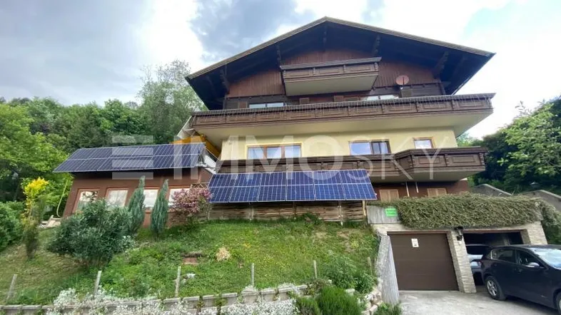 Mehrstöckiges Haus mit traditioneller Holzfassade, Balkonen und Solaranlagen auf dem Dach.