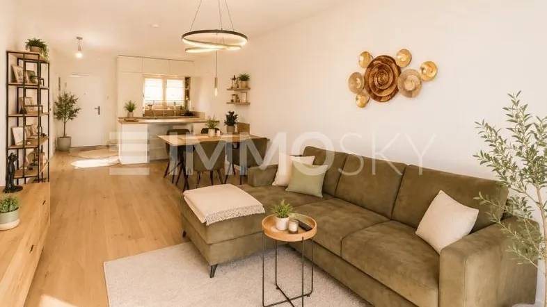 Helles, offenes Wohnzimmer mit bequemer Couch, Holzboden und integrierter Küche mit Essbereich.