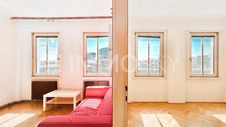 Helles Wohnzimmer mit Parkettboden, rotem Sofa und weitem Blick auf die Stadt.