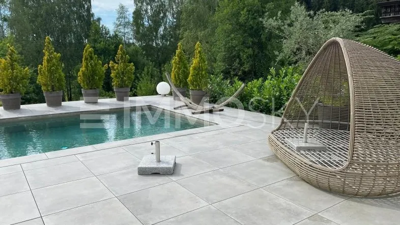 Gepflegter Außenbereich mit Swimmingpool, gefliester Terrasse und bequemen Outdoor-Möbeln, umgeben von viel Grün.