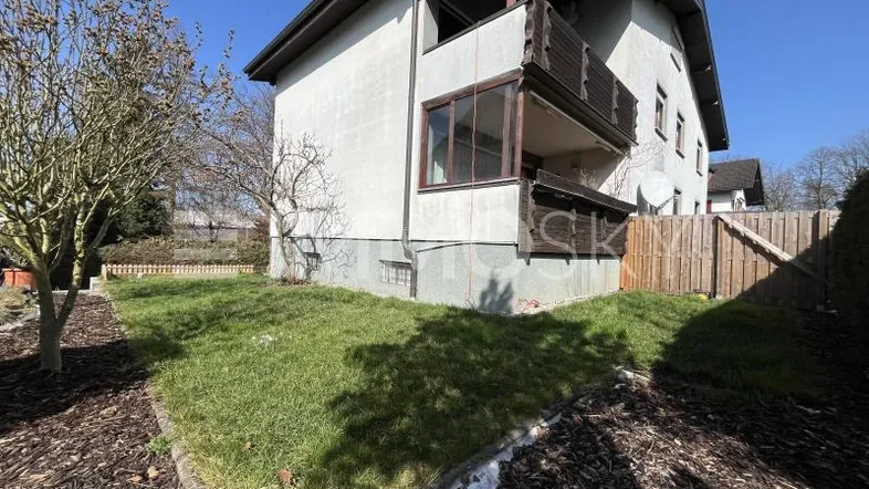 Seitenansicht des Hauses mit kleinem Gartenbereich, Rasenfläche und einem Balkon im Obergeschoss.