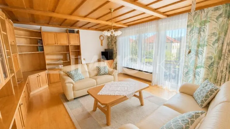 Geräumiges Wohnzimmer mit Holzbalkendecke, Parkettboden und großen Fenstern mit Blick ins Grüne.