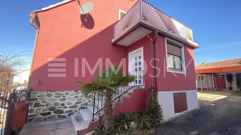 Rotes Haus mit Steinsockel, Außentreppe und Satellitenschüssel unter blauem Himmel.