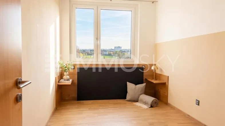 Helles Schlafzimmer mit Holzboden, großem Fenster und Blick ins Grüne.