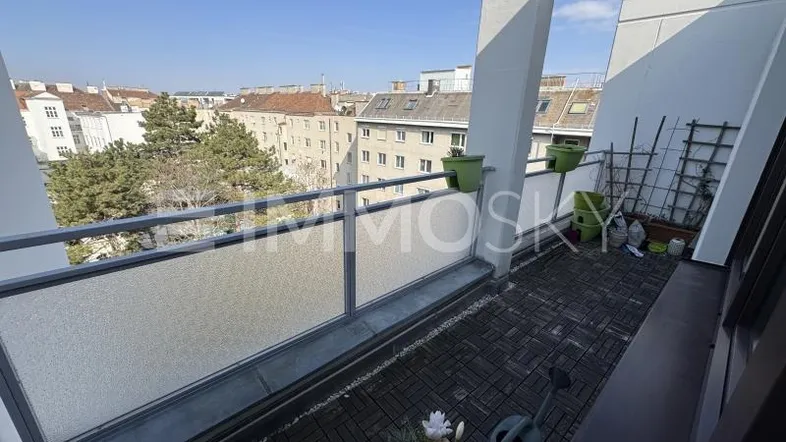 Geräumiger Balkon mit Holzboden und weitem Blick über die Stadt und umliegende Gebäude.