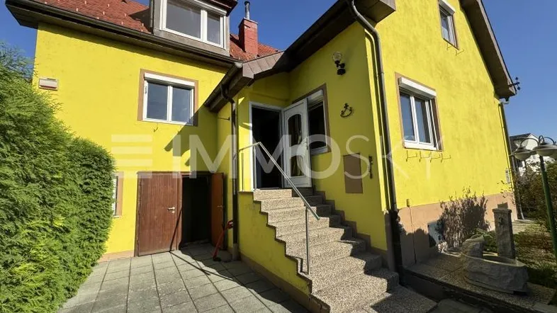 Gelbe Hausfassade mit Außentreppe und Eingangsbereich unter blauem Himmel.