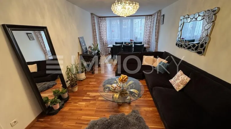 Geräumiger Wohn- und Essbereich mit dunklem Sofa, Holzboden und einem eleganten Kronleuchter.
