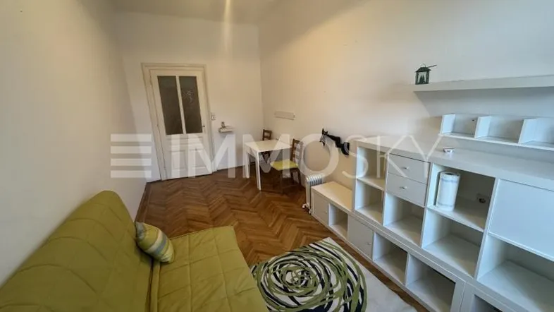 Gemütlicher Wohnbereich mit grünem Sofa, Holzparkettboden und einem kleinen Esstisch.