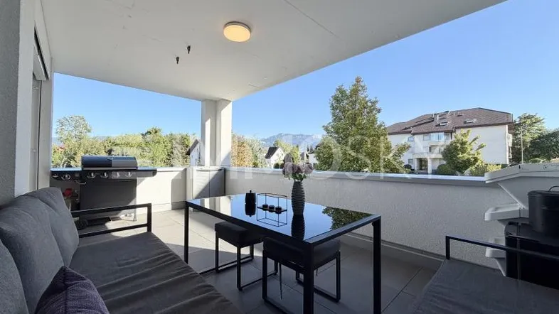 Geräumiger Balkon mit bequemen Outdoor-Möbeln, Grill und weitem Blick ins Grüne und auf die Berge.