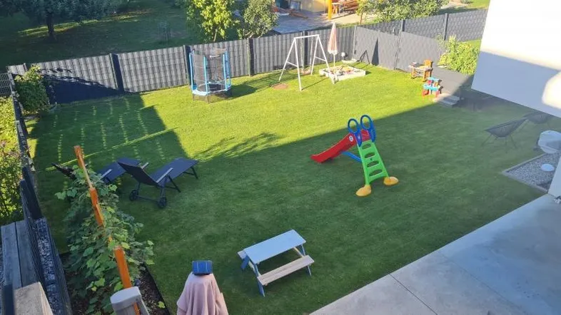 Großer Garten mit Rasenfläche, Trampolin, Rutsche und Schaukel für Kinder.