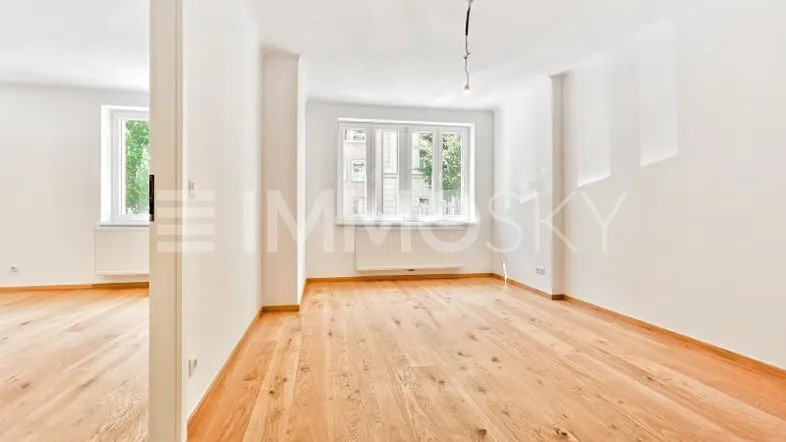 Helles Zimmer mit Holzboden und weißen Wänden, bietet viel natürliches Licht durch die Fenster.