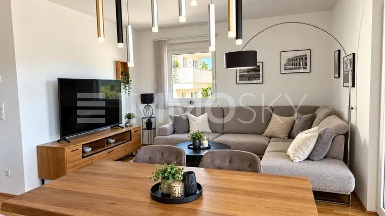 Moderner offener Wohn-Essbereich mit Holztisch, bequemer Couch und stilvoller Beleuchtung.