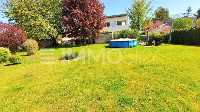 Großer, gepflegter Garten mit Rasenfläche, Bäumen und einem kleinen Aufstellpool hinter dem Haus.