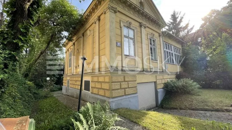 Historisches gelbes Gebäude mit klassischer Architektur, umgeben von üppigem Grün und einem Gartenbereich.