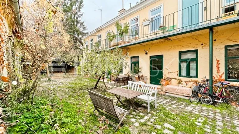 Grüner Innenhof mit Gartenmöbeln und Balkonen an der gelben Gebäudefassade.