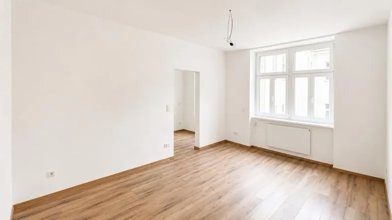 Heller, leerer Raum mit Laminatboden, weißen Wänden und großem Fenster, bereit zum Einzug.