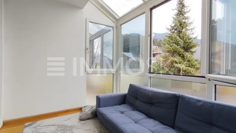 Heller Wintergarten mit Glasdach, gemütlichem Sofa und Blick auf die umliegende Natur.