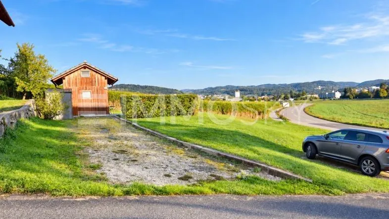Blick auf ein kleines Holzgebäude mit Schotterparkplatz und weitem Blick über die grüne Landschaft.