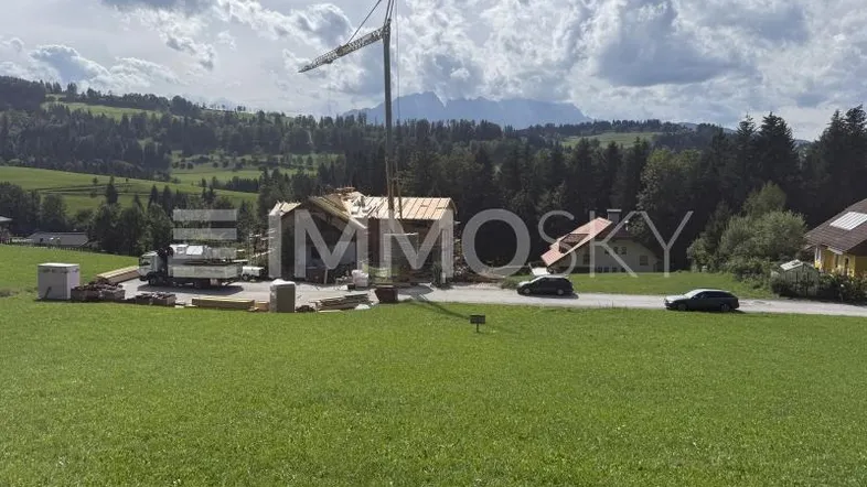 Baustelle eines neuen Gebäudes in ländlicher Umgebung mit Bergblick unter bewölktem Himmel.