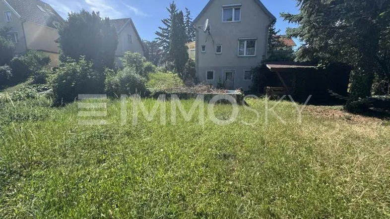 Hinteransicht eines Wohnhauses mit großem, verwildertem Gartenbereich unter blauem Himmel.