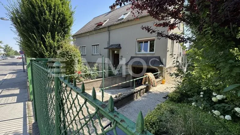 Vorderansicht eines Hauses mit grünem Zaun, Vorgarten und einer Rampe zum Eingang.