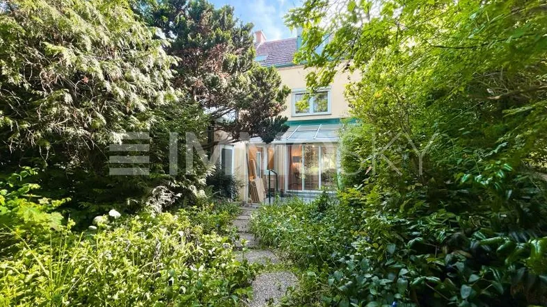 Blick vom üppigen Garten auf das Haus mit Wintergarten und grünem Umfeld.