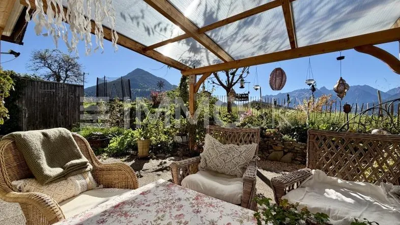 Überdachte Terrasse mit Korbmöbeln und einem malerischen Bergblick, ideal zum Entspannen im Freien.