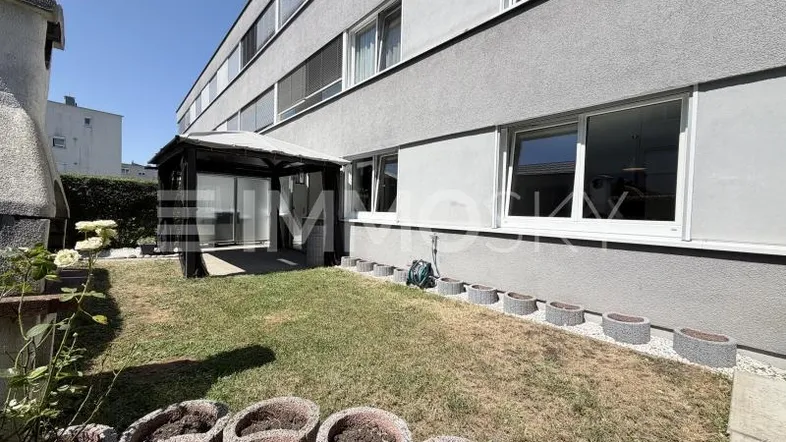 Außenansicht des Gebäudes mit kleinem Gartenbereich und überdachtem Sitzplatz im Freien.
