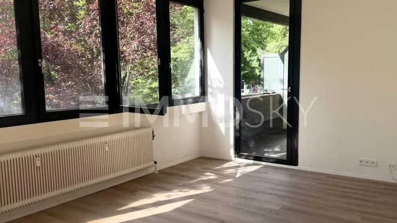 Helles Zimmer mit großen Fenstern, Laminatboden und Zugang zum Außenbereich.