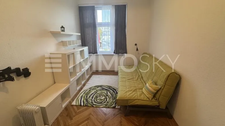Helles Zimmer mit Parkettboden, einem Sofa und einem Regal, ideal als Wohn- oder Gästezimmer.