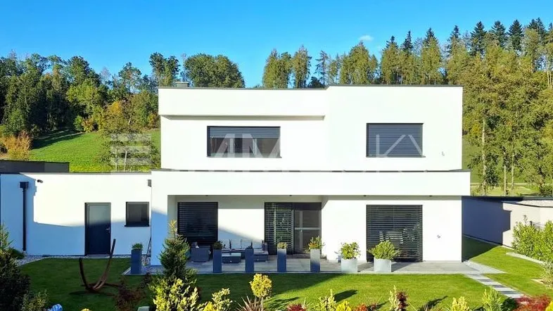Moderne weiße Villa mit Flachdach, gepflegtem Garten und möblierter Terrasse im Grünen.