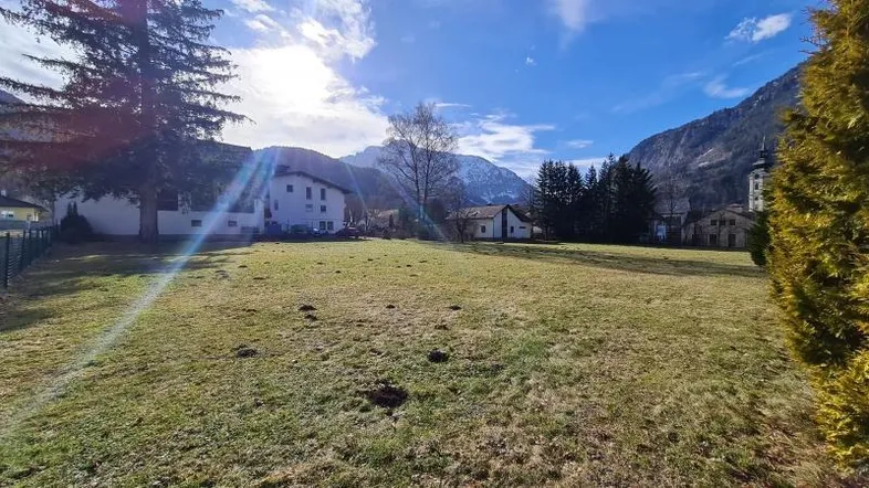 Weitläufige Grünfläche mit Blick auf umliegende Häuser und schneebedeckte Berge unter blauem Himmel.