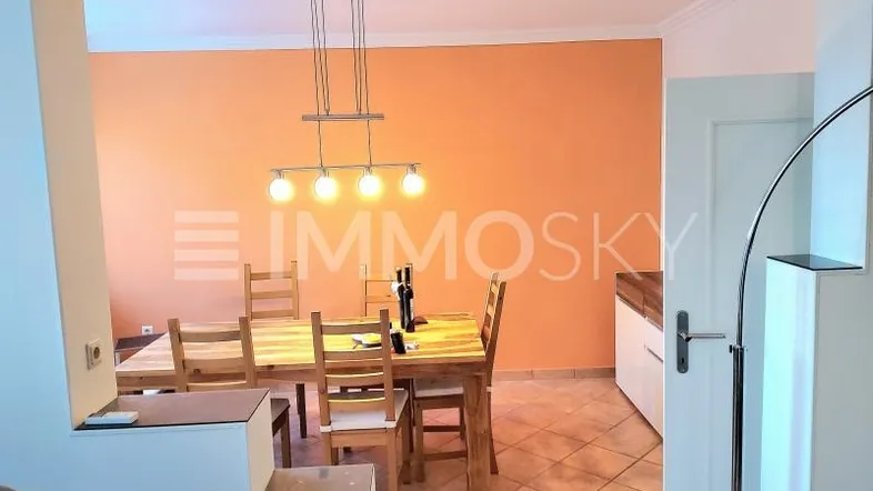Heller Essbereich mit Holztisch, Stühlen und einer auffälligen orangefarbenen Wandgestaltung.