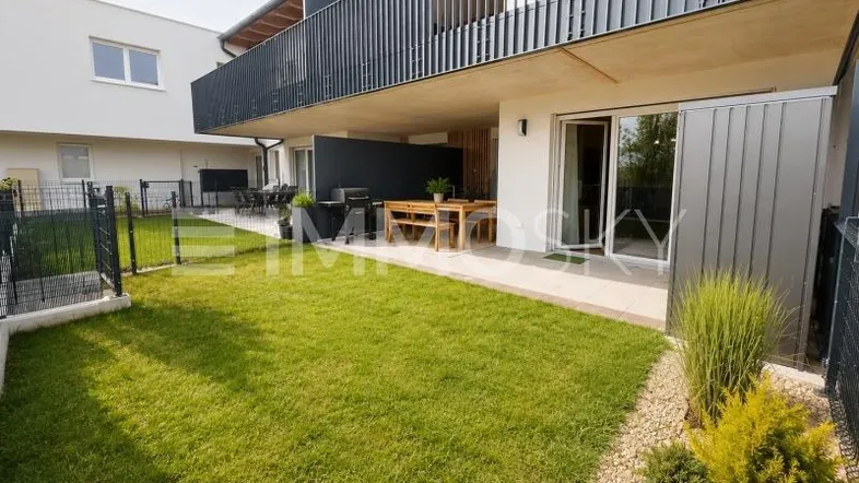 Gepflegter Gartenbereich mit Rasenfläche und möblierter Terrasse vor einem modernen Gebäude.